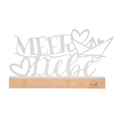 Weißer Deko-Aufsteller mit dem Schriftzug „Meer Liebe“ und Herz-Boot-Motiv auf einem Holzsockel mit UNUS® HOME Logo, freigestellt vor weißem Hintergrund.
