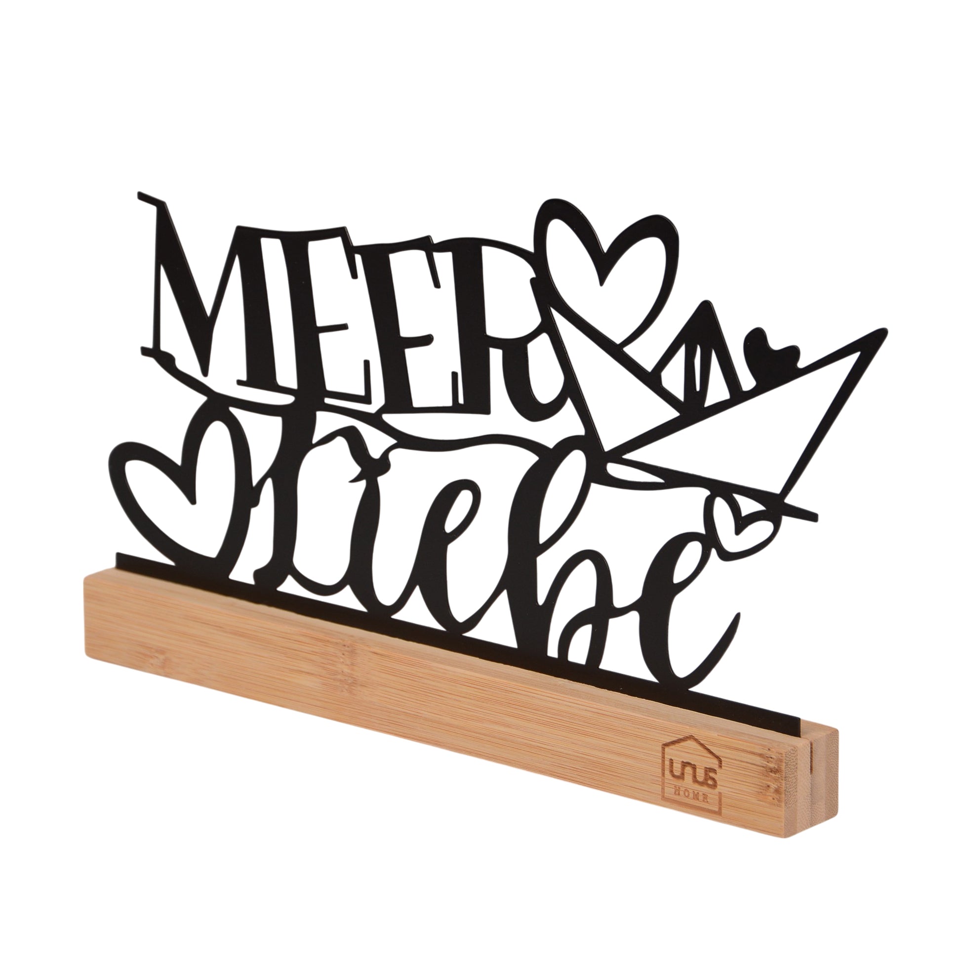 Freigestellter seitlicher Blick auf den schwarzen Schriftzug „Meer Liebe“ mit Herz und Papierboot auf einem naturfarbenen Holzsockel mit UNUS-Logo.